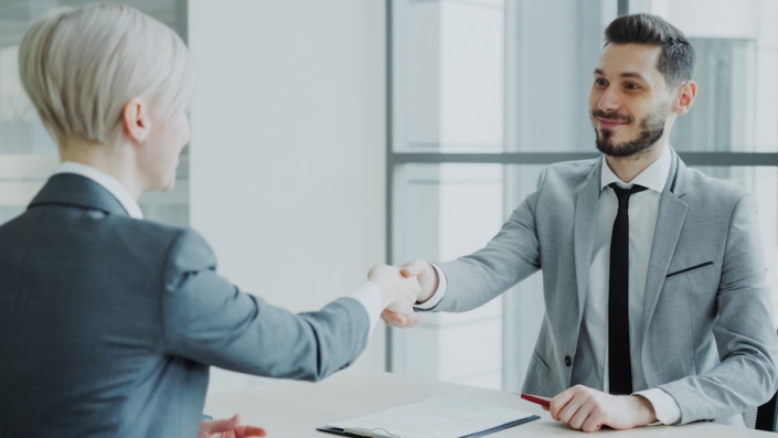 visory-a-people Two professionals shaking hands across a desk after a job interview